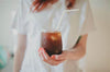 A woman in a white shirt holding a glass of iced coffee.