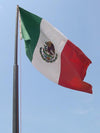 The flag of mexico, featuring the colors red, white and green, flying beneath a blue sky.